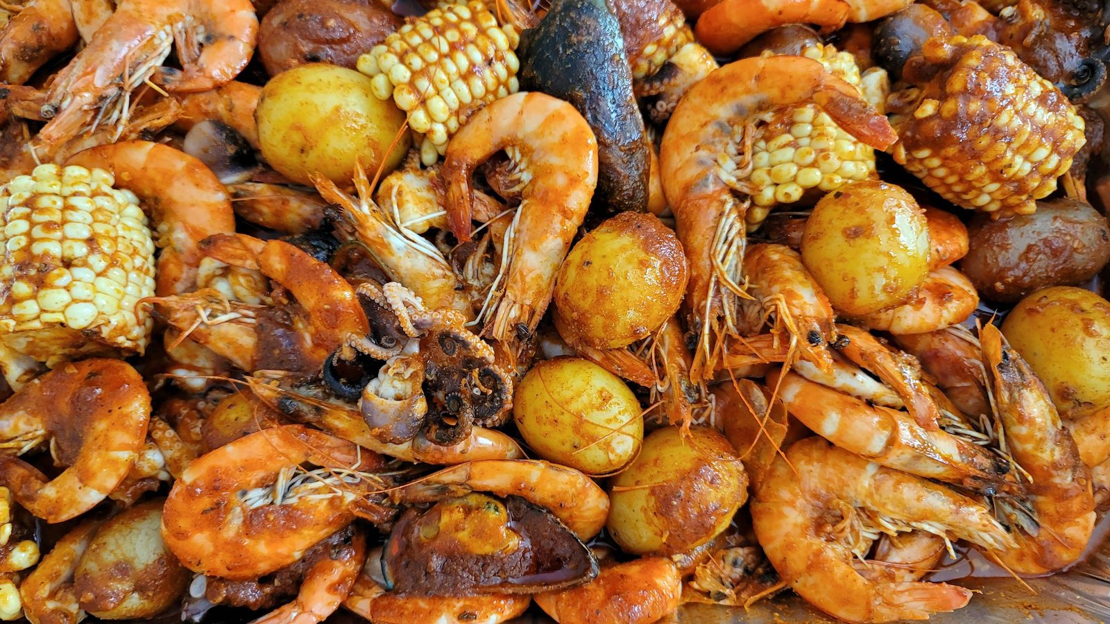 Close overhead view of a glossy seafood boil with shrimp, corn, potatoes and mussels