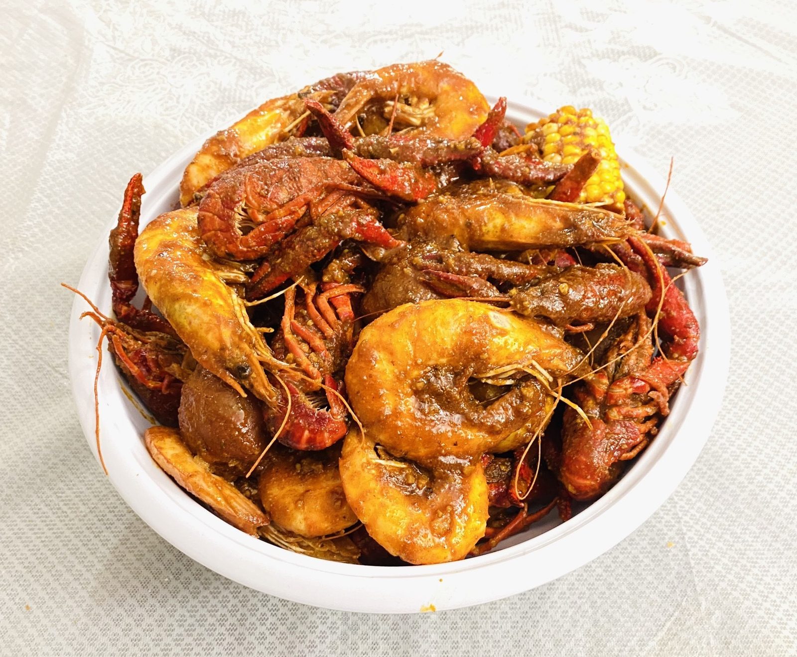 Saucy shrimp, sausage, corn and potatoes served on a white platter